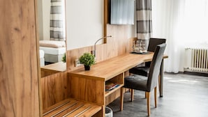 A modern room with a wooden desk, a chair, a TV mounted on the wall, and a window with curtains. - Landhotel Georgshof (Huenfeld)