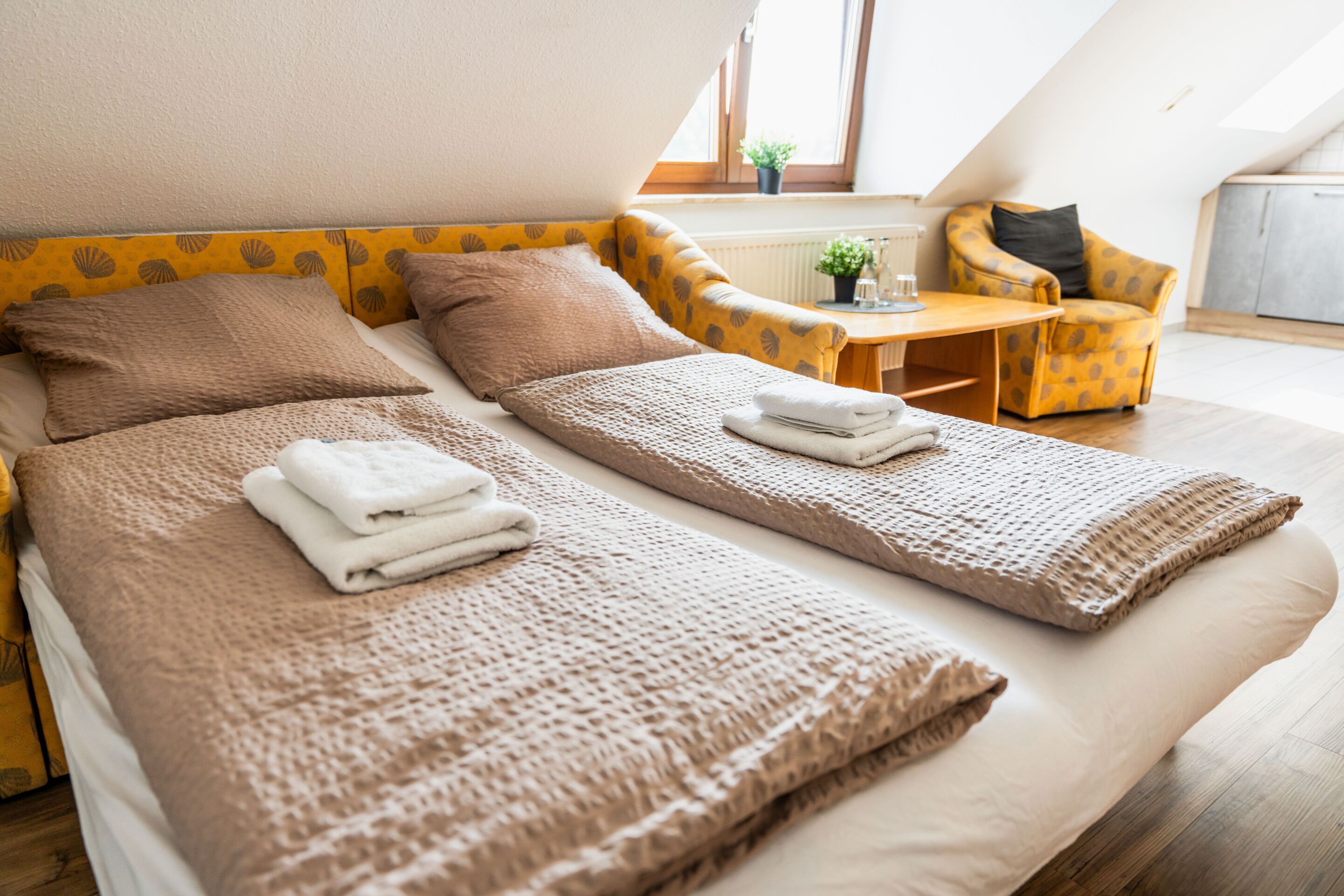 Habitación de hotel moderna con dos camas individuales, una pequeña mesa, una silla y un ventanal con vistas.
