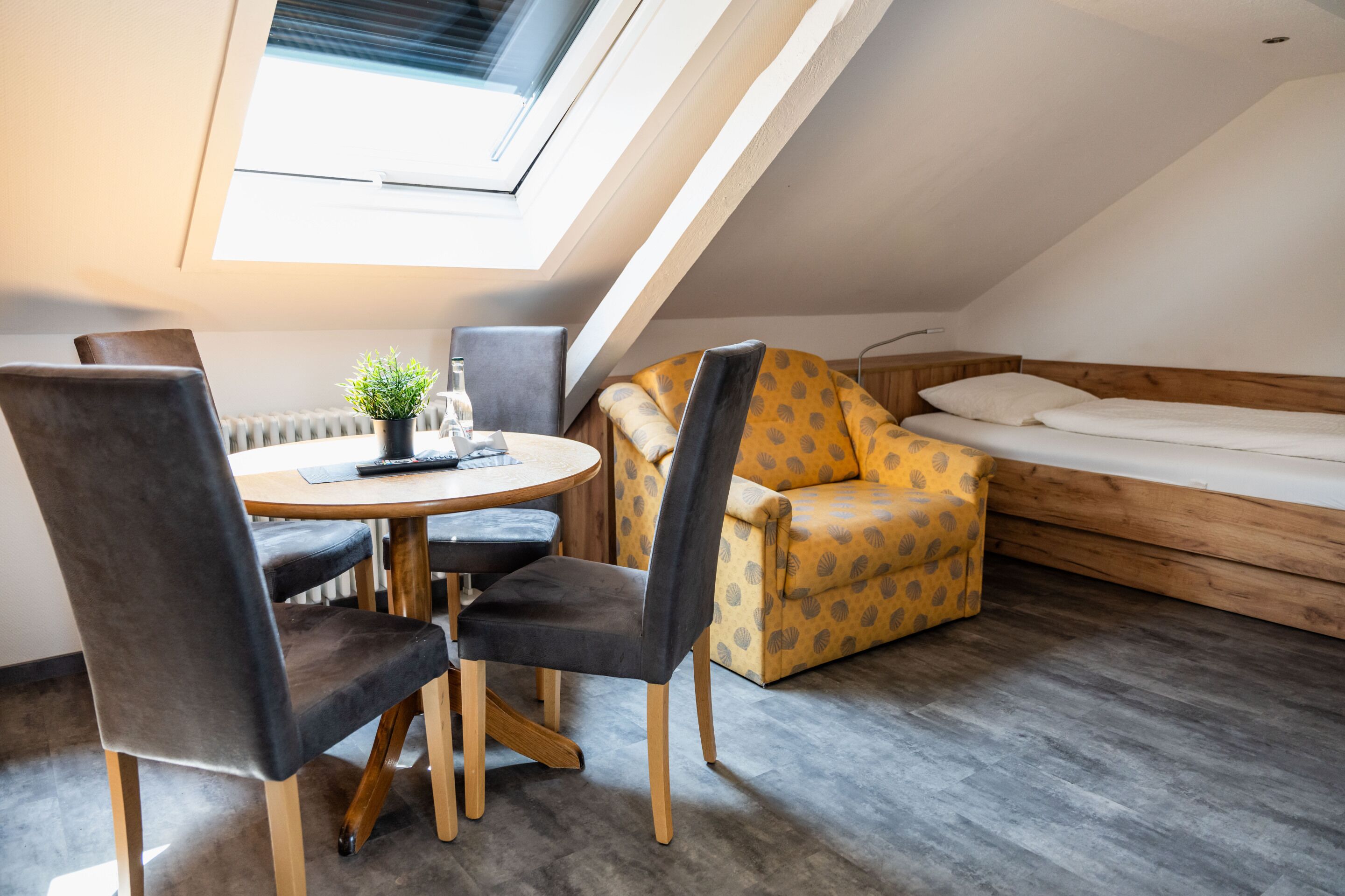 Una habitación acogedora con un tragaluz, una mesa redonda de comedor con sillas, un sofá y una cama.