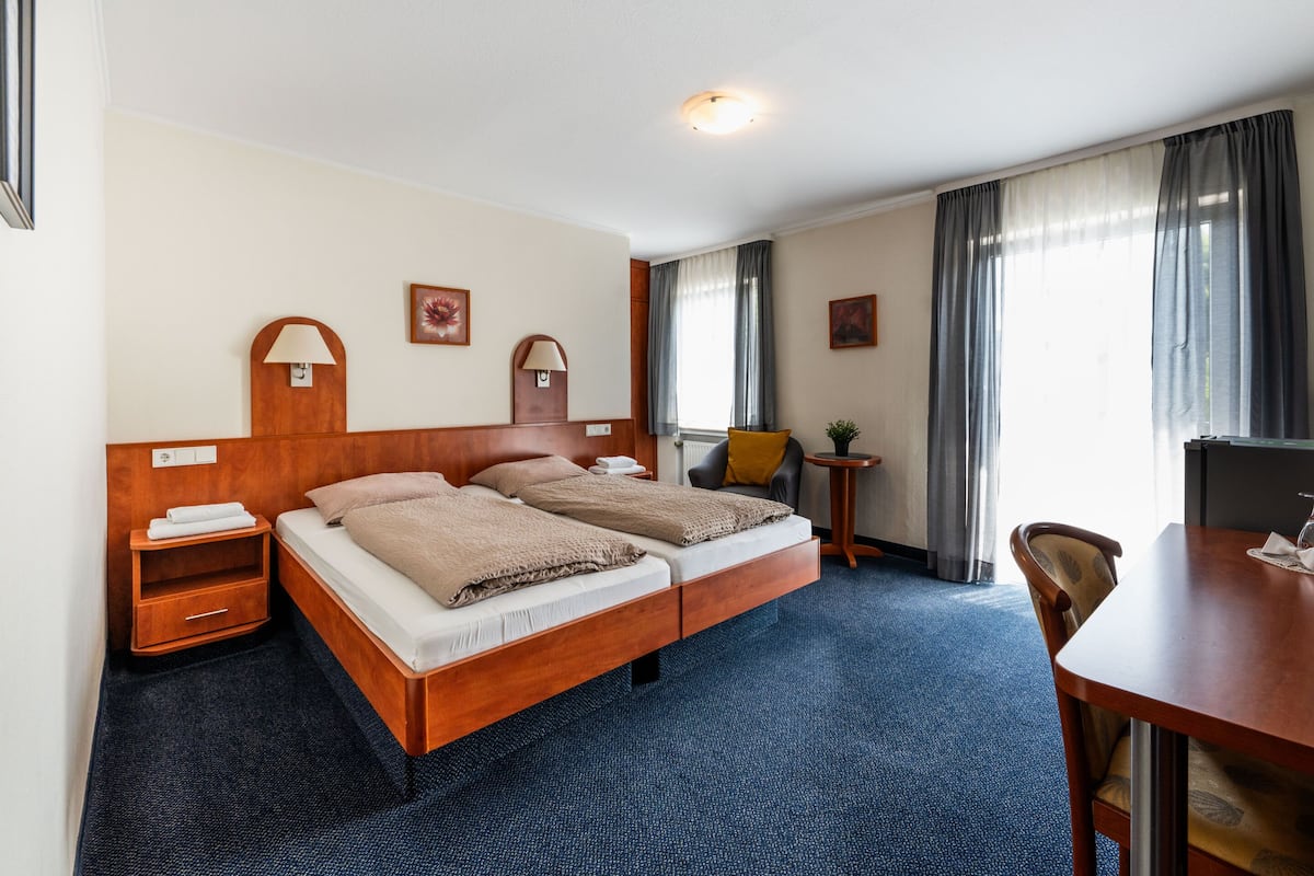 A hotel room with a double bed, a desk, a chair, a small table, and a lamp.