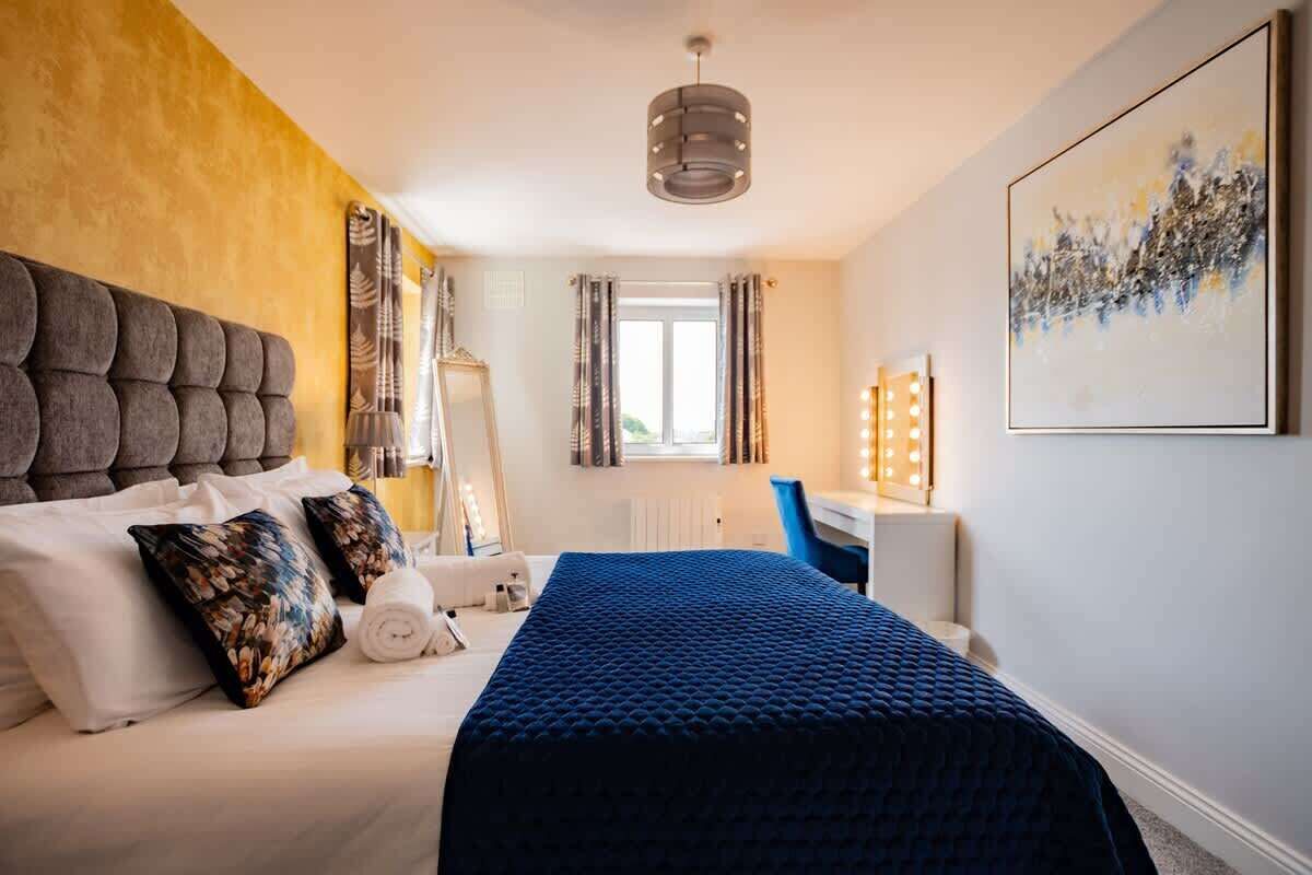 Ett hotellrum med en stor säng, ett skrivbord med en stol, ett fönster med gardiner och en taklampa.