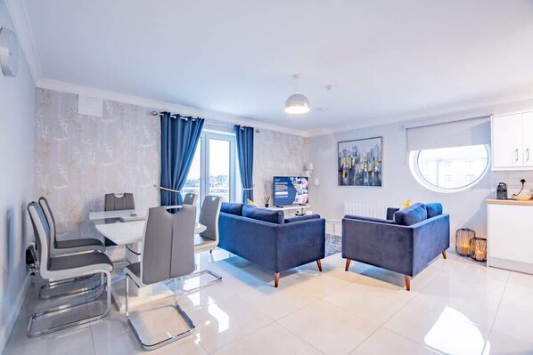 A modern living room with a dining area, two sofas, a TV, and a kitchen area.