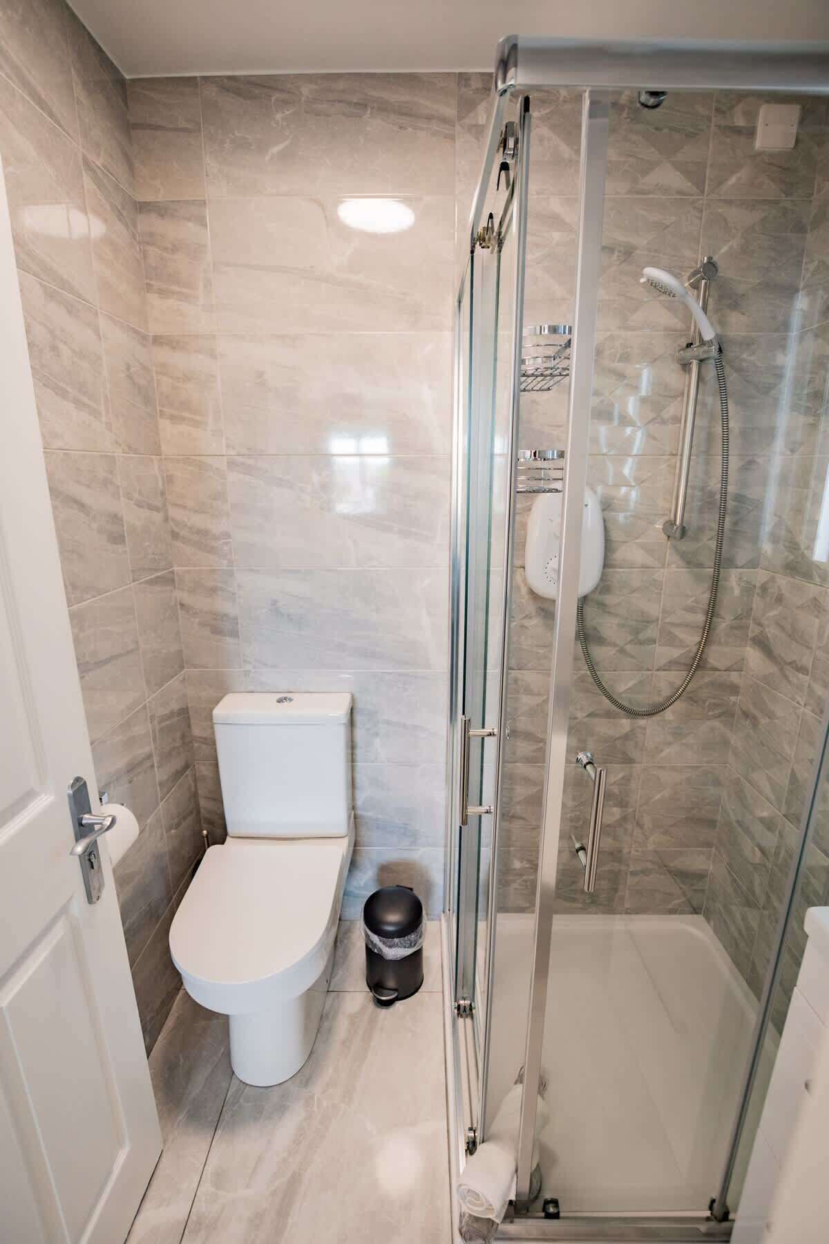 Ett modernt badrum med en dusch som är avskärmad med glasväggar, en toalett och en papperskorg.