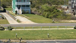 Un edificio a due piani con tetto verde e facciata bianca, situato vicino a una strada con un'area verde di fronte.