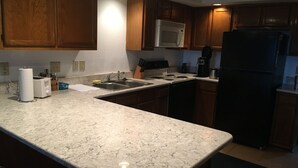 Una cucina con mobili in legno, un forno a microonde bianco, un frigorifero nero e un piano di lavoro in marmo.