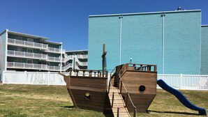 Un'area giochi a tema pirata con una struttura in legno, uno scivolo e circondata da prato e recinzione bianca.