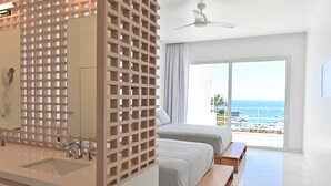 A modern hotel room with a large balcony, a ceiling fan, and a view of the sea.