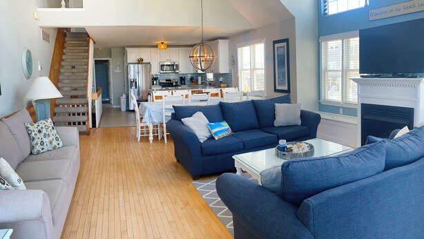 A spacious living area with a blue sofa, a white sofa, and a coffee table. There is a kitchen in the background with white cabinets and a hanging light fixture. - Beautiful 4-bedroom, beach block home in Sea Isle City!  (Sea Isle City)