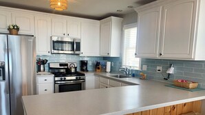 A modern kitchen with white cabinets, stainless steel appliances, a large island with bar stools, and a window providing natural light. - Beautiful 4-bedroom, beach block home in Sea Isle City!  (Sea Isle City)