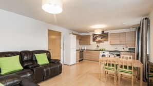 Eine moderne Wohnung mit Wohnbereich, ausgestattet mit einem Ledersofa und einem Esstisch mit Stühlen. Die Küche verfügt über Holzschränke, einen Kühlschrank und eine Mikrowelle.