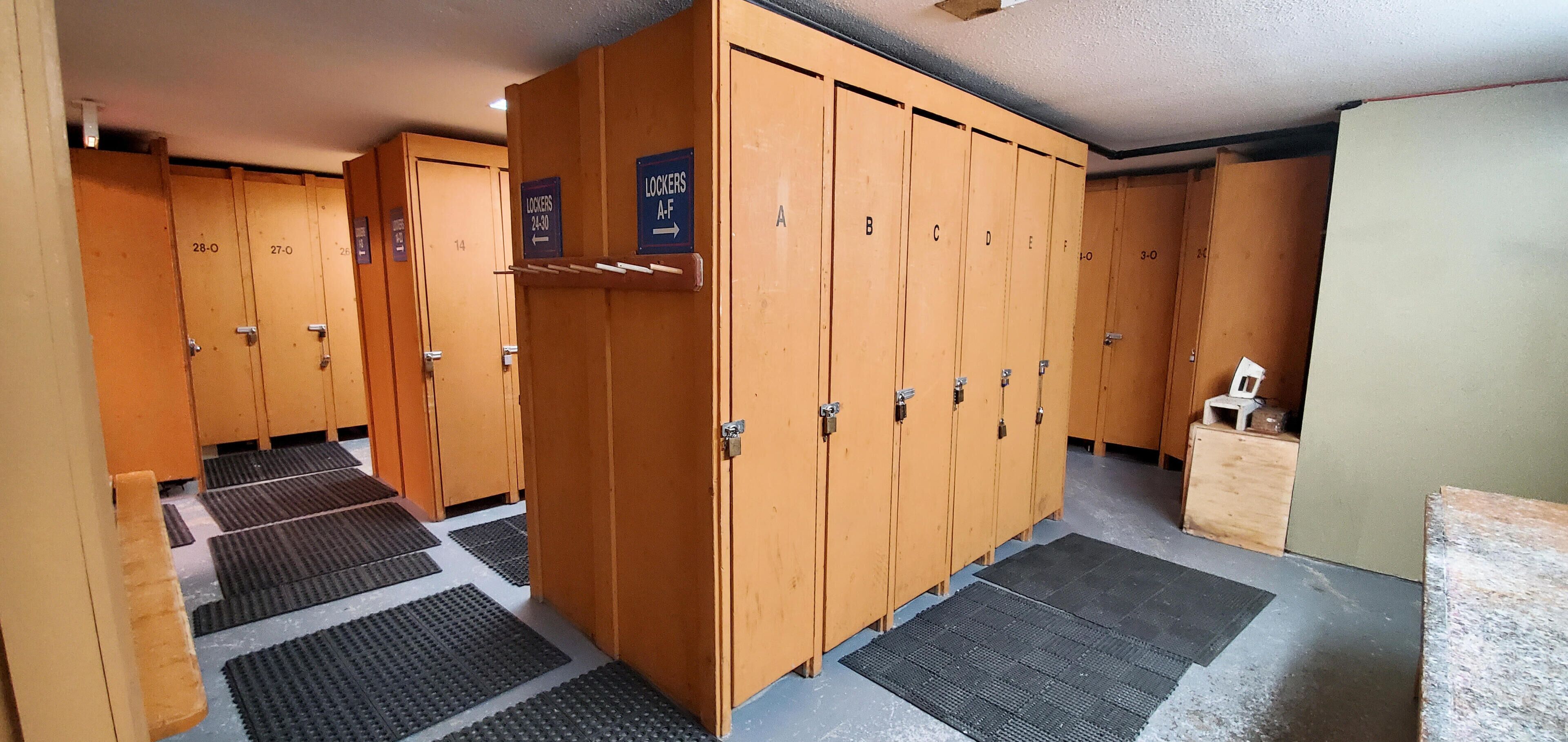 A row of wooden lockers with numbered doors, a sign indicating lockers are available 24/7, and a small wooden cabinet to the right.
