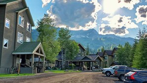 A residential area with houses, a dirt road, parked cars, and mountains in the background. - Open Plan Living Area, 2 Q Beds, Full Kitchen, Walk to Trails, Portable AC (Fernie)