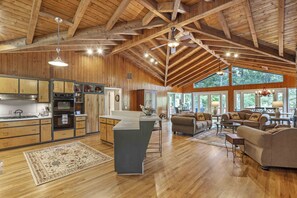 Une cuisine spacieuse avec des meubles en bois, un îlot central et une grande fenêtre donnant sur une forêt.