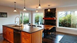 A modern kitchen with a large island, wooden cabinets, a built-in dishwasher, and pendant lighting. - BayView House, Tofino B.C. (Tofino)