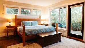 A bedroom with a bed, two bedside tables, a bench, and large windows offering a view of greenery. - BayView House, Tofino B.C. (Tofino)