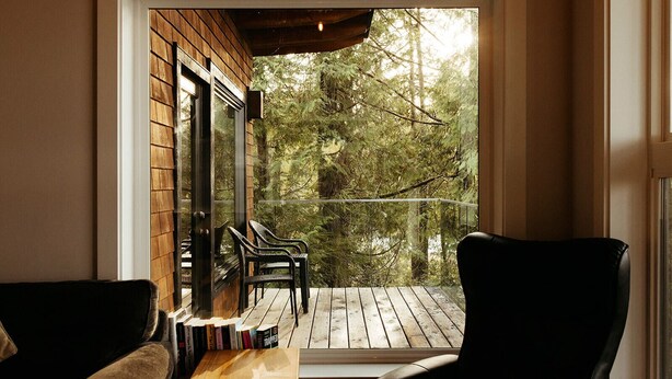 A cozy reading nook with a wooden table and chairs, overlooking a wooden deck and dense forest. - BayView House, Tofino B.C. (Tofino)
