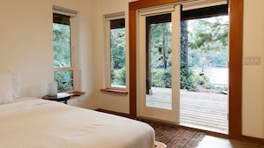 A bedroom with a large bed, two windows, and a view of a garden. - Cozy home in Tofino w/ hottub (Tofino)