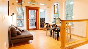 A cozy living room with a sofa, dining table, chairs, and a staircase leading to a balcony. - Cozy home in Tofino w/ hottub (Tofino)