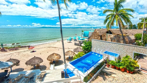 Ein Strandhotel mit Schwimmbad, Liegestühlen und Reetdachschirmen.