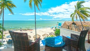 Ein Balkon mit Korbmöbeln, der auf einen Strand mit Palmen und einen klaren Meerblick blickt.