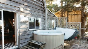 Una cabaña de madera con jacuzzi, terraza y zona de estar exterior cubierta.