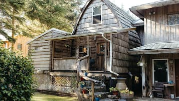 Une maison rustique en bois, dotée d’un porche, d’un escalier en pierre et de plantes en pot.