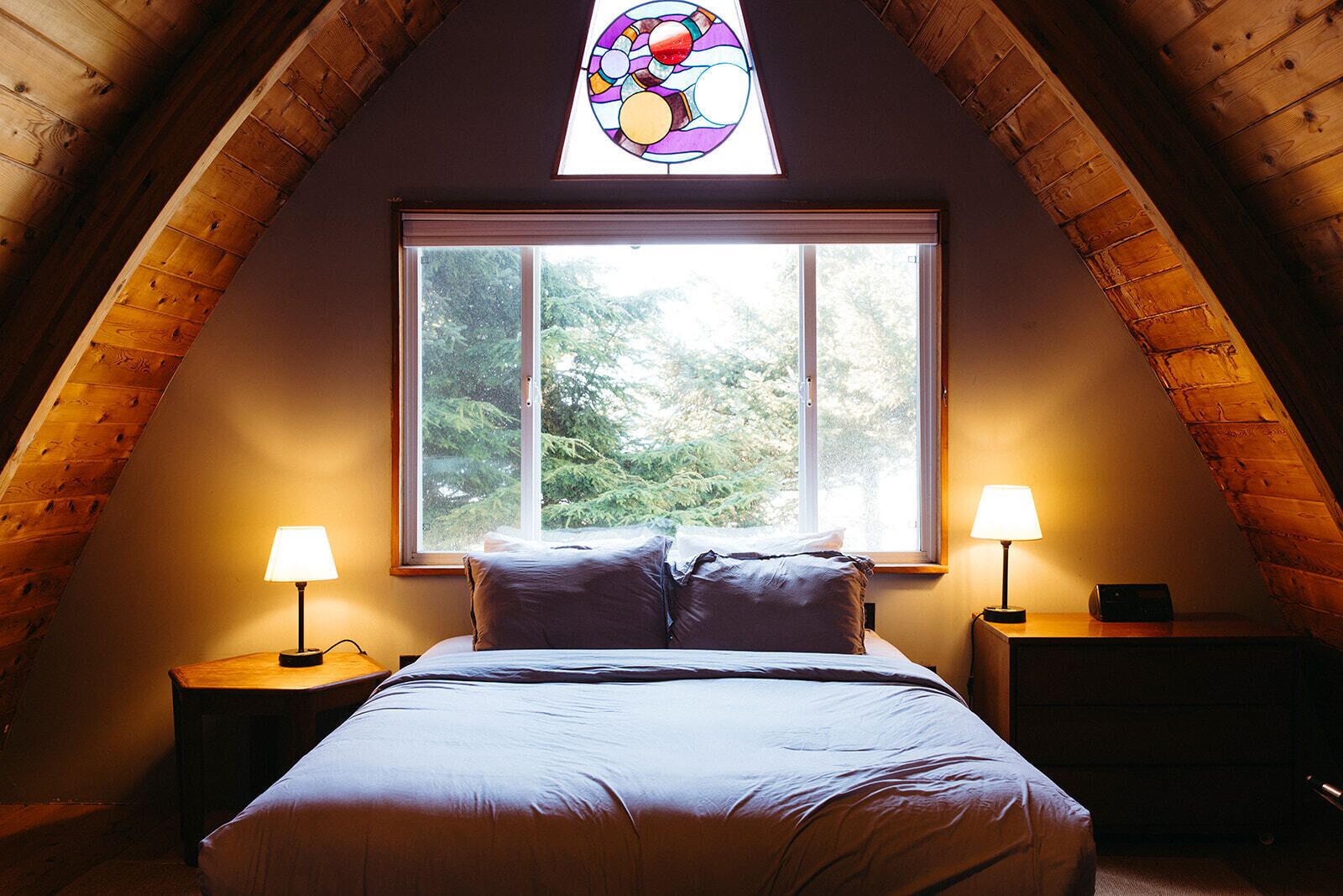 Une chambre confortable avec une grande fenêtre, deux lampes de chevet et un vitrail au-dessus du lit.