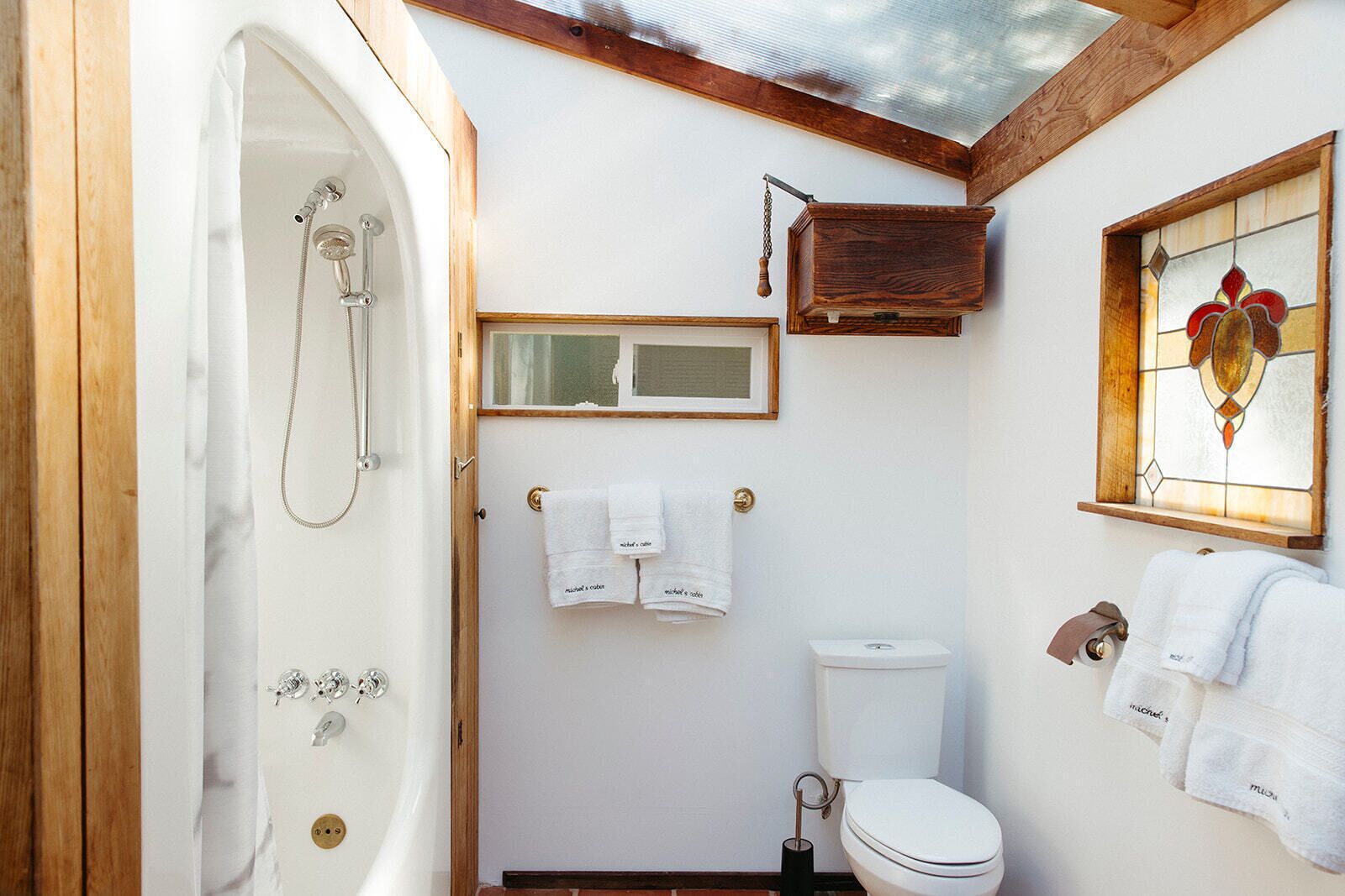 A bathroom with a bathtub, toilet, and a small window with stained glass.