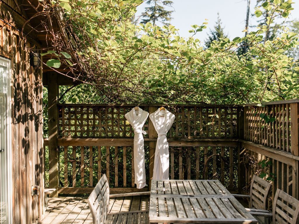 An outdoor wooden deck with a table and chairs, surrounded by a wooden fence and lush greenery.