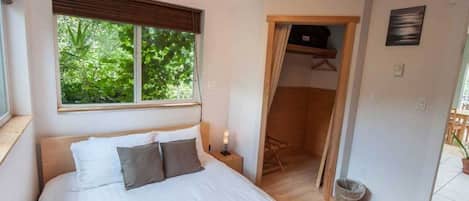 A bedroom with a bed, a window, a closet, and a door leading to an outdoor area.