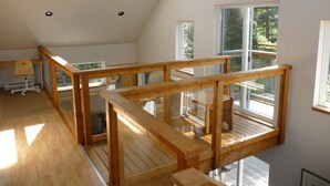 Amplo quarto no estilo loft com varanda de madeira, claraboias e grandes janelas que oferecem vista para o exterior.