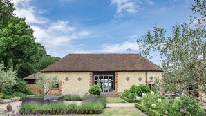 A brick building with a tiled roof, a front door, and a small garden with various plants and a pathway leading to the entrance. - Stunning 6 bedroom converted barn nestled in Souths Downs; 5,000+ sq ft; 9 acres (Storrington)