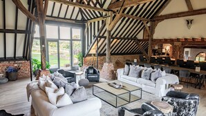 A spacious living area with a high ceiling and exposed beams, furnished with sofas and a coffee table, and a view of the outdoors. - Stunning 6 bedroom converted barn nestled in Souths Downs; 5,000+ sq ft; 9 acres (Storrington)