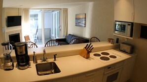 A compact kitchen with a sink, stove, and microwave. There is a dining area with a table and chairs visible through an open door. - The Yacht House, Tofino B.C. (Tofino)