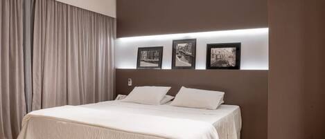 Une chambre à coucher moderne avec un grand lit, une tête de lit dotée de lampes fixées au mur et un rideau sur le côté gauche.