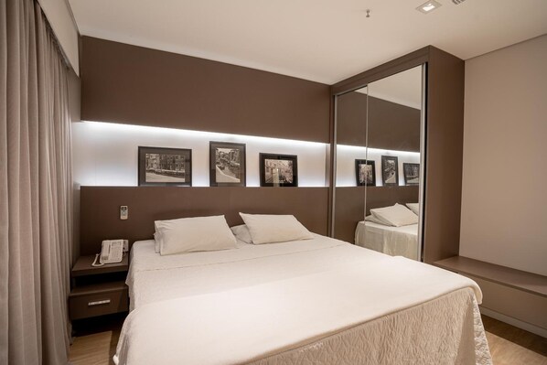 A modern hotel room with a large bed, bedside tables, a phone, and framed pictures on the wall. - Zahara Hotel (Limeira)