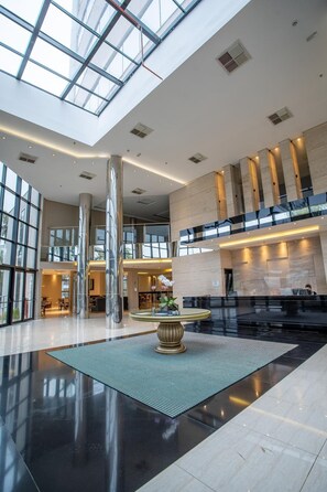 A spacious lobby with a high ceiling, large windows, and a central reception desk. - Zahara Hotel (Limeira)