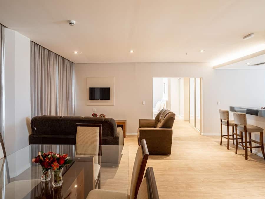 A modern living room with a glass dining table, sofas, and a TV mounted on the wall.