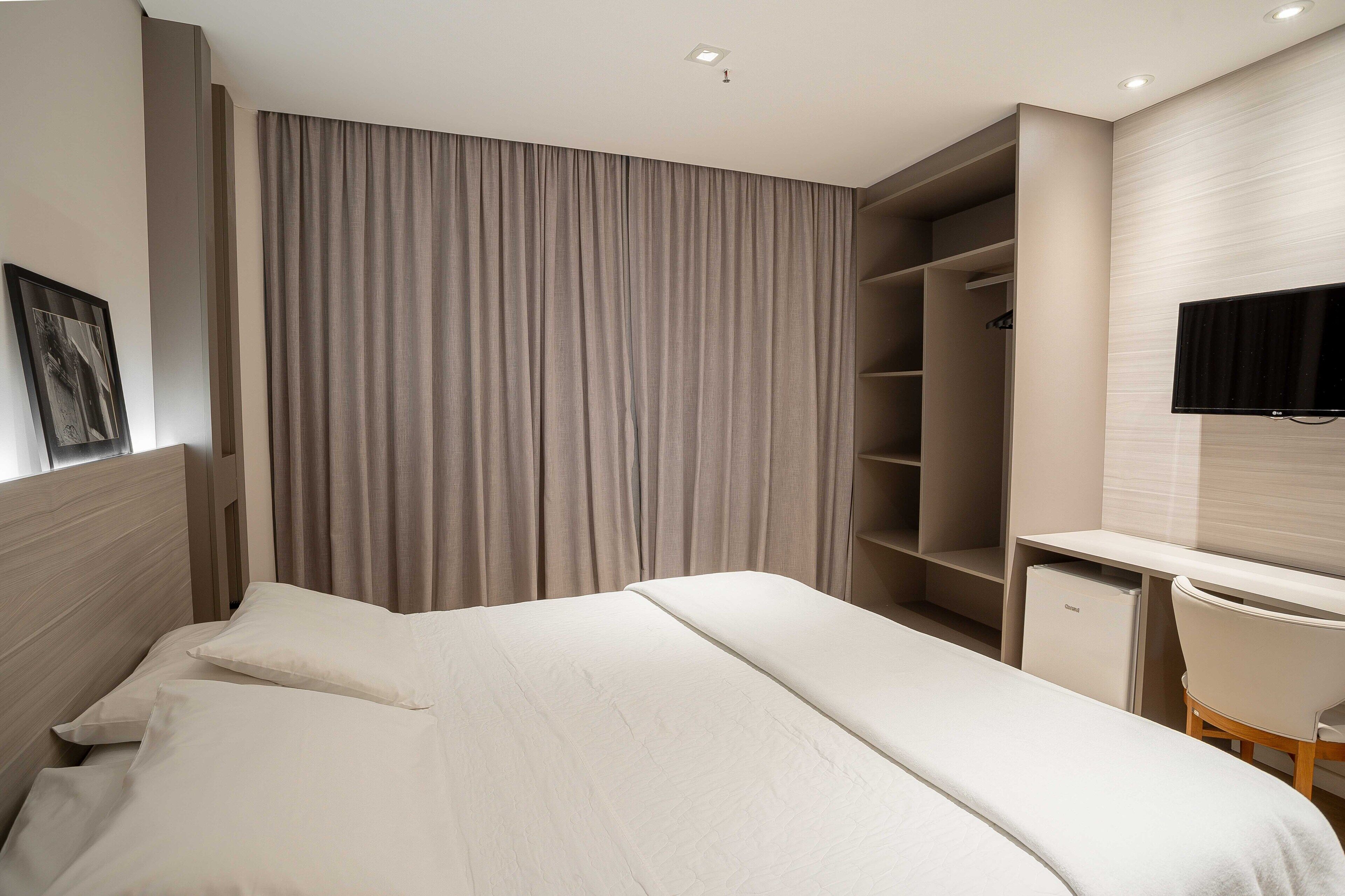Una habitación de hotel moderna con una cama grande, un escritorio, un televisor y un armario.