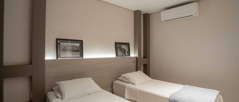 Habitación de hotel con dos camas individuales, un cabecero, un aire acondicionado de pared y dos cuadros enmarcados.