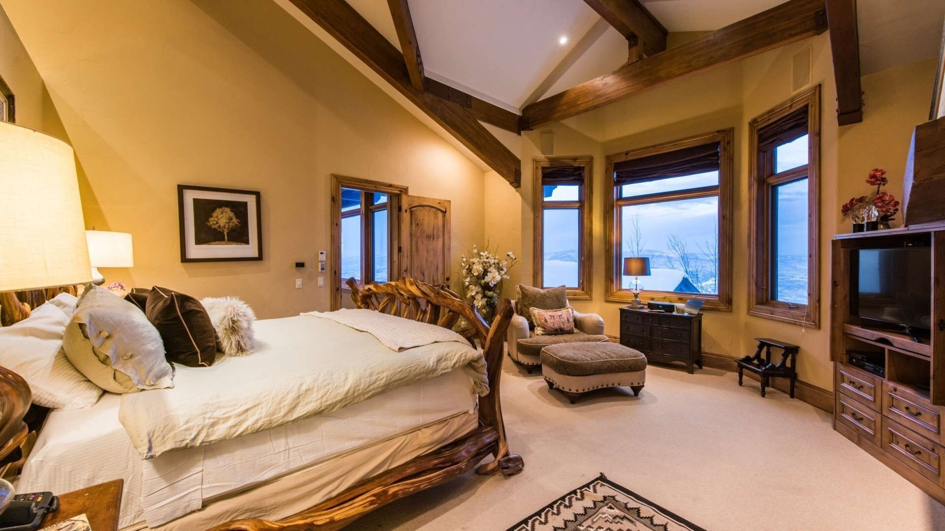 Een slaapkamer met een groot bed, een houten hoofdbord, een nachtkastje, een dressoir en een televisie.