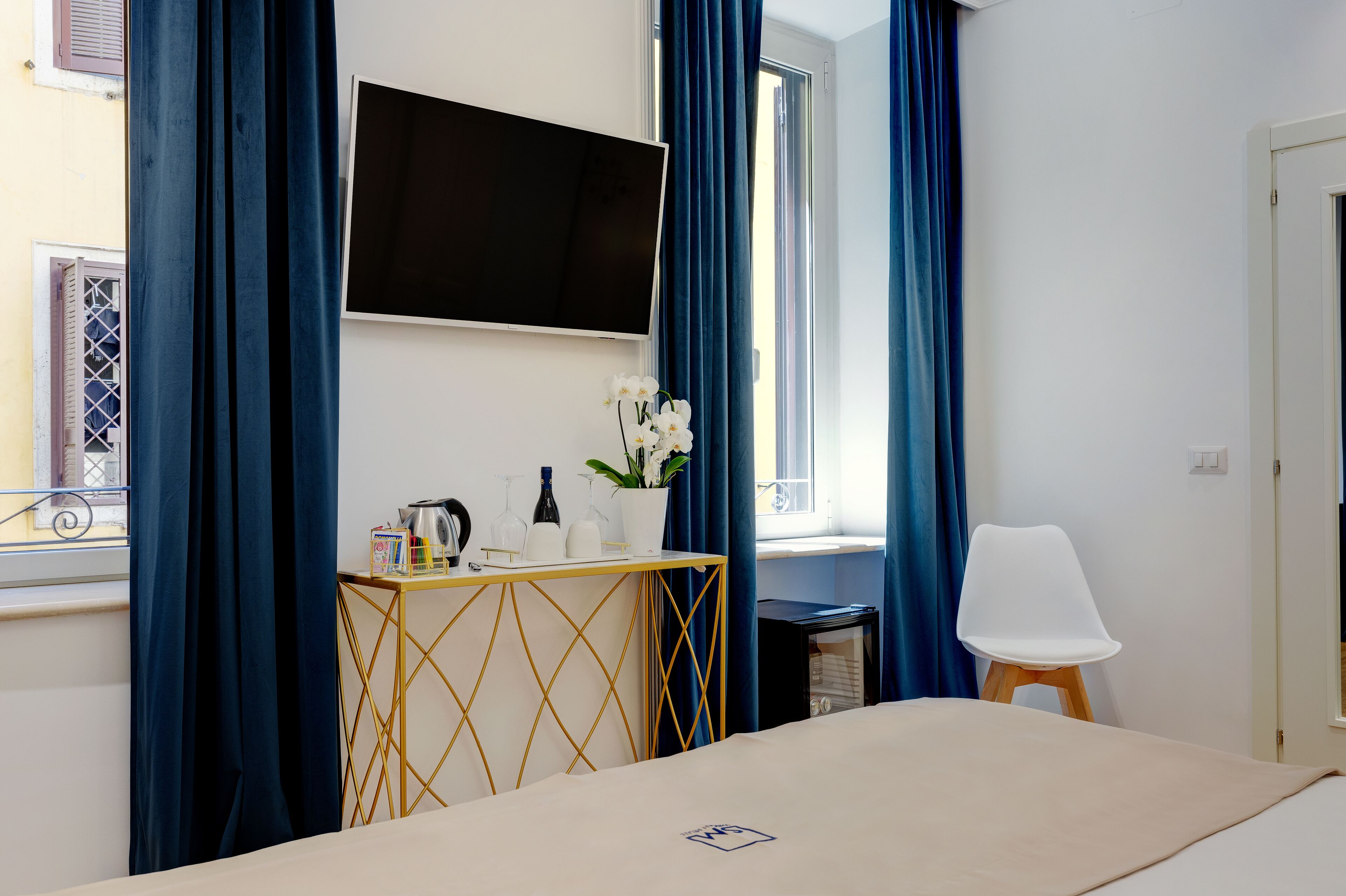 A hotel room with a bed, a TV mounted on the wall, a small table with a vase of flowers, and a chair.