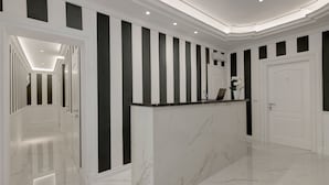 Uma área de recepção com balcão de mármore, paredes com listras pretas e brancas e um design de teto moderno.