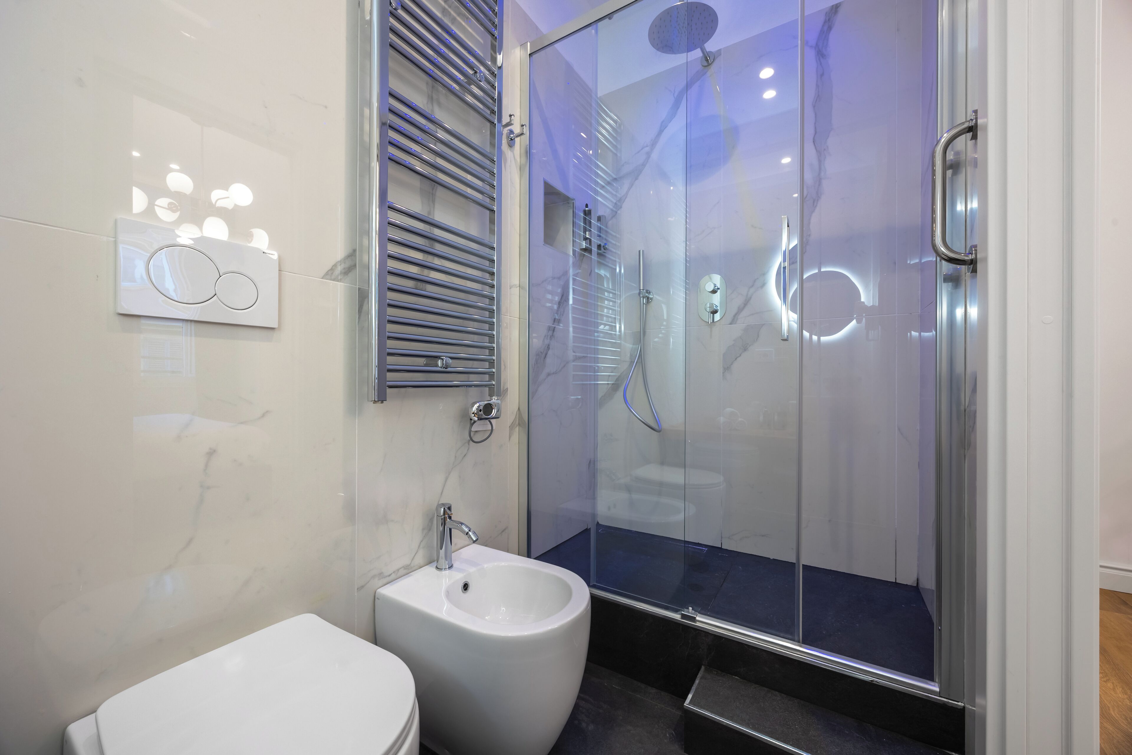 A modern bathroom with a glass-enclosed shower, a white pedestal sink, and a marble-tiled wall.
