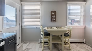 A dining area with a table and chairs, two windows with blinds, a wall-mounted sign, and a door with a view of buildings outside. - 2026 LAVALLETTE NEW Kitchen and Bathroom, Outdoor Shower & BEACH BADGES INCLUDED (Lavallette)