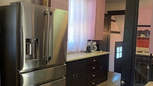 A compact kitchen with stainless steel appliances, a dining area with a wooden table and chairs, and a tiled floor.