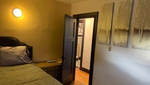 A bedroom with a bed, a bedside table, a nightstand, a door, and a wall with three framed pictures.