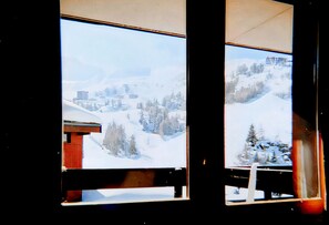Une vue sur un paysage montagneux enneigé, aperçue à travers une fenêtre à cadre en bois.