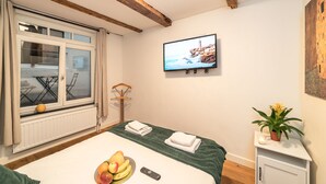 A hotel room with a bed, a television, a window with curtains, a radiator, and a small table with a plant. - Dutch House (Amsterdam)