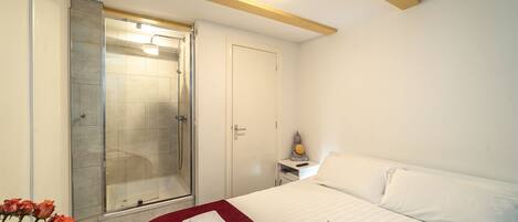 Una habitación de hotel con cama, mesita de noche, ducha y puerta.